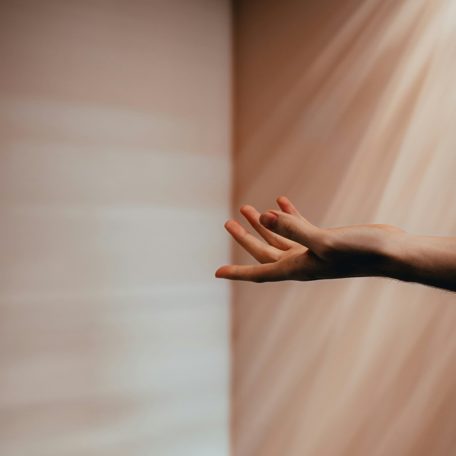 An open hand reaching into soft light against a warm wall