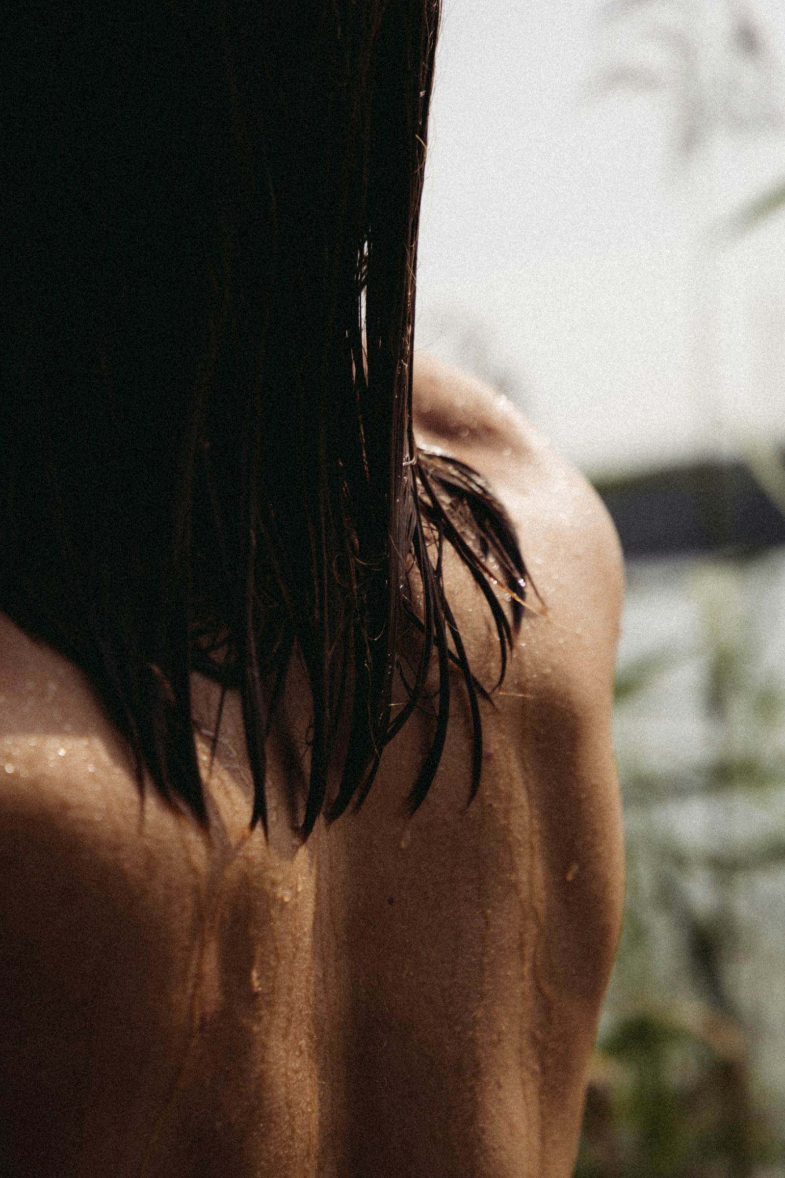 Sunlight on a woman's back and wet hair, greenery beyond