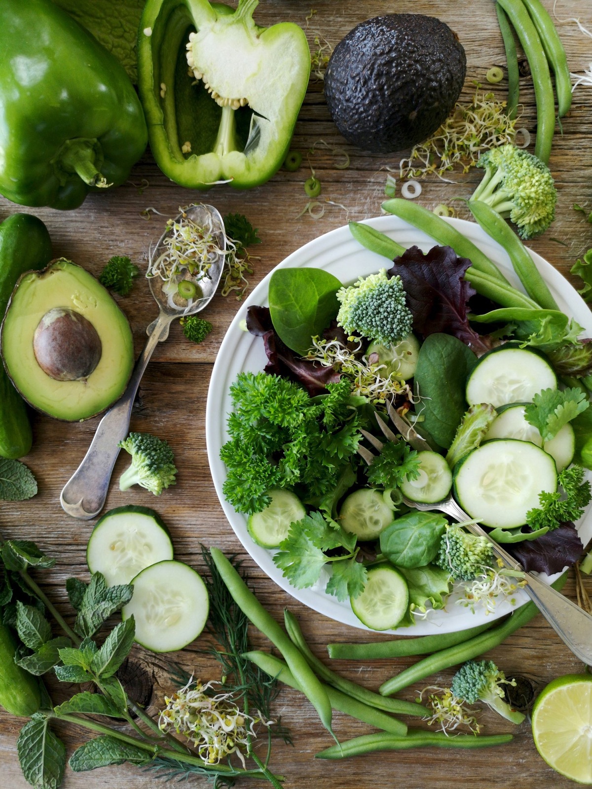 A flat lay of green vegetables — avocado, broccoli, cucumber and herbs